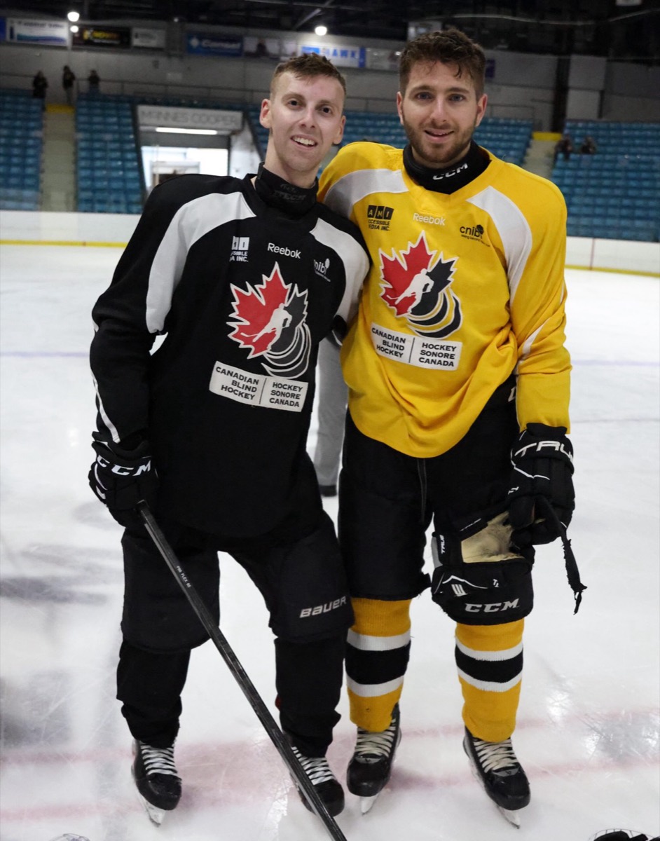 Two players, one in a black jersey and one in a yellow jersey, standing together on the ice