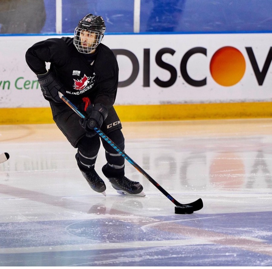 A player in a black Blind Hockey jersey skating with the puck in a full-size arena