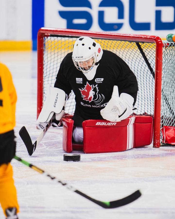 A young goalie in a white helmet and Blind Hockey jersey crouched in the net, watching the puck